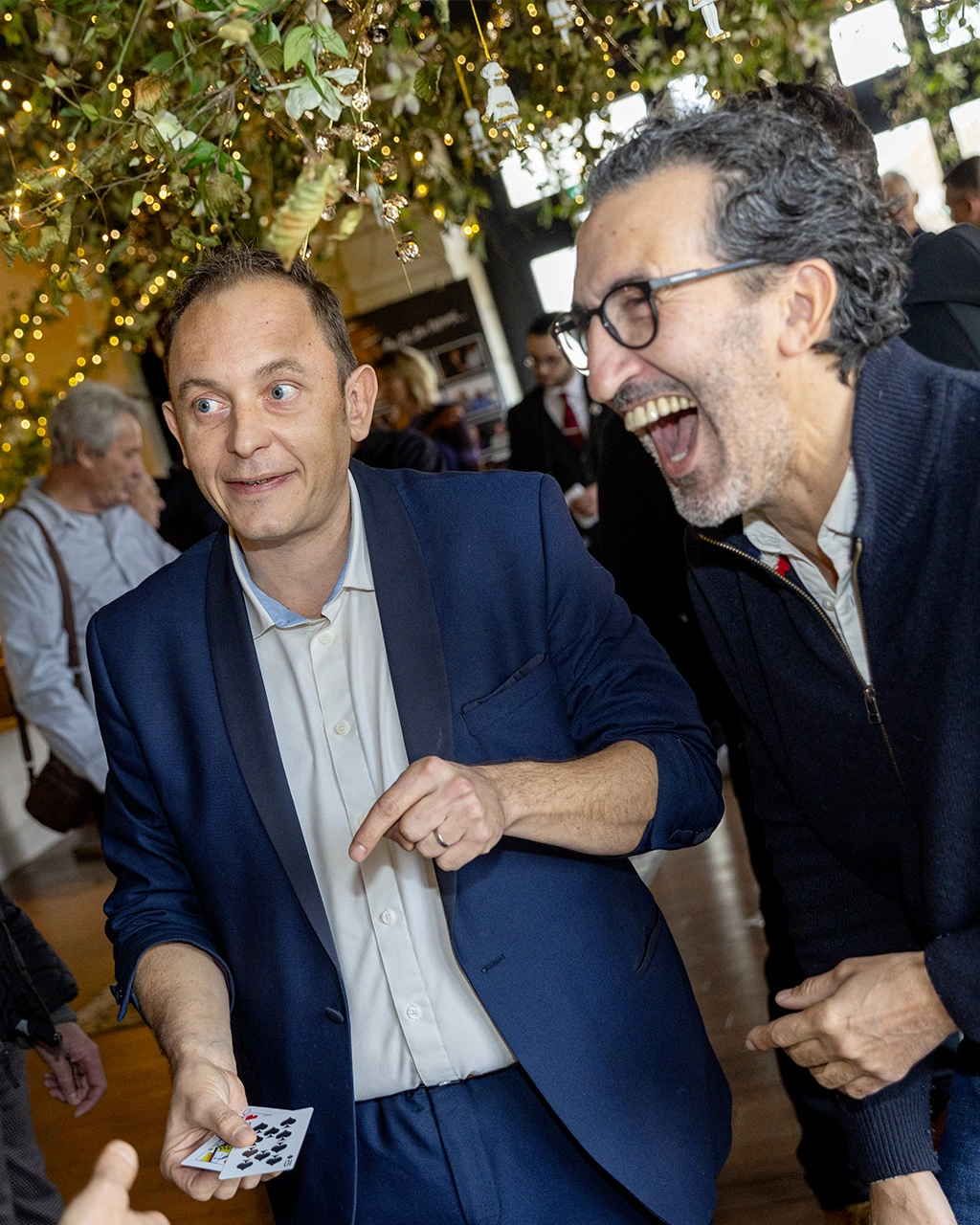 Grégory présente une carte lors d'un cocktail, un invité éclate de rire derrière lui